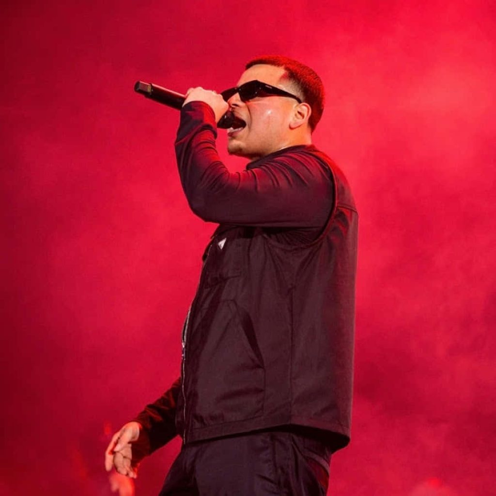 Fuerza Regida lead singer Jesús Ortiz Paz performing live on stage with red background wallpaper