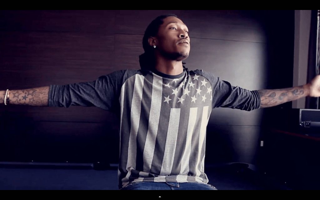 Future rapper with tattoos in American flag shirt posing confidently in dark studio background Wallpaper