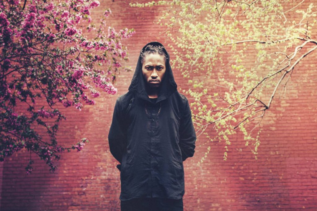 Future rapper in black hoodie with intense gaze pink blossoms green branches urban style wallpaper