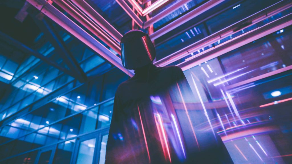 Mysterious figure in futuristic helmet inside neon-lit glass city with blue and magenta lights Wallpaper