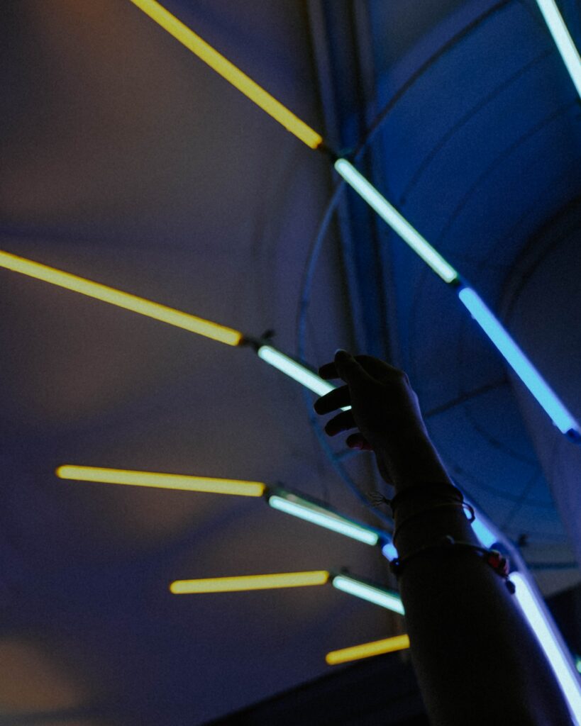 Silhouetted hand reaching glowing neon tubes blue yellow futuristic radiant dark background wallpaper