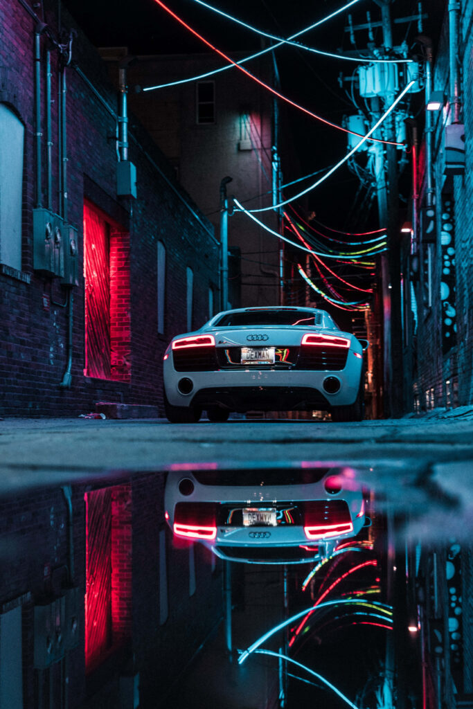 White supercar in neon-lit narrow alley with vibrant reflections on wet urban street background Wallpaper