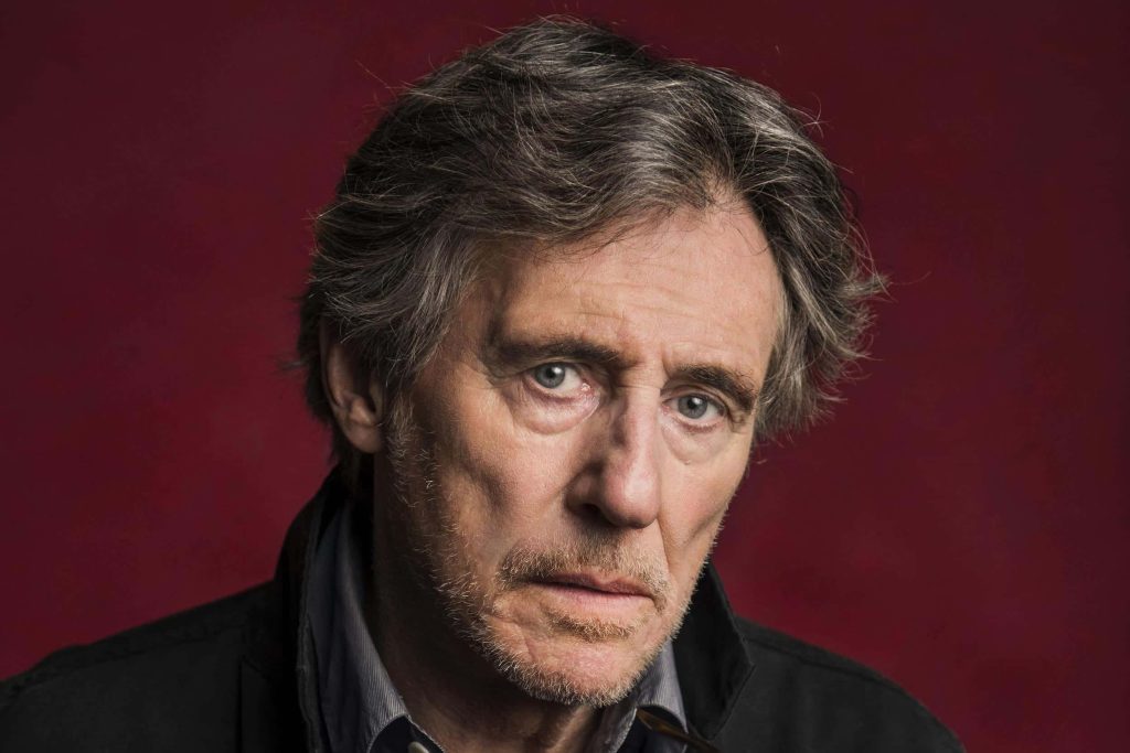 Gabriel Byrne portrait with grey hair and piercing gaze on dramatic deep red background wallpaper