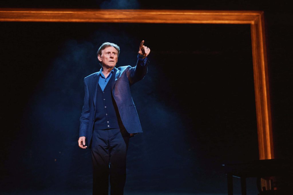 Gabriel Byrne in dark suit pointing upward dramatic lighting moody background cinematic wallpaper