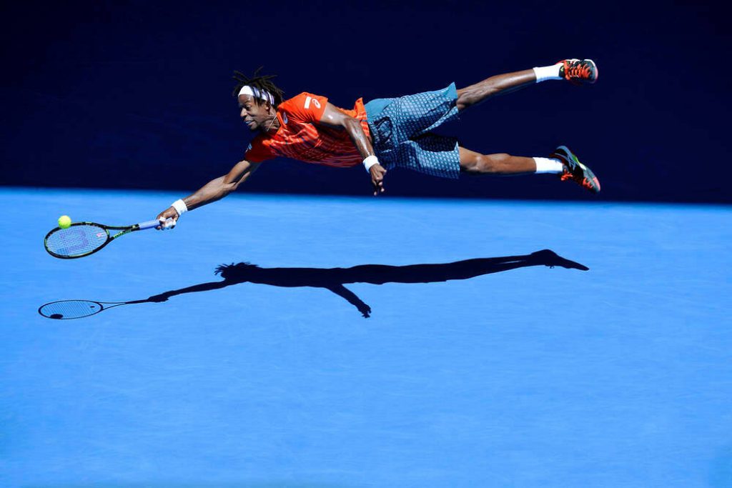 Gaël Monfils diving mid-air on vibrant blue tennis court high-energy action wallpaper