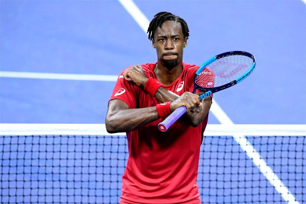 Tennis star Gaël Monfils in red shirt on blue court holding racket with arms crossed wallpaper