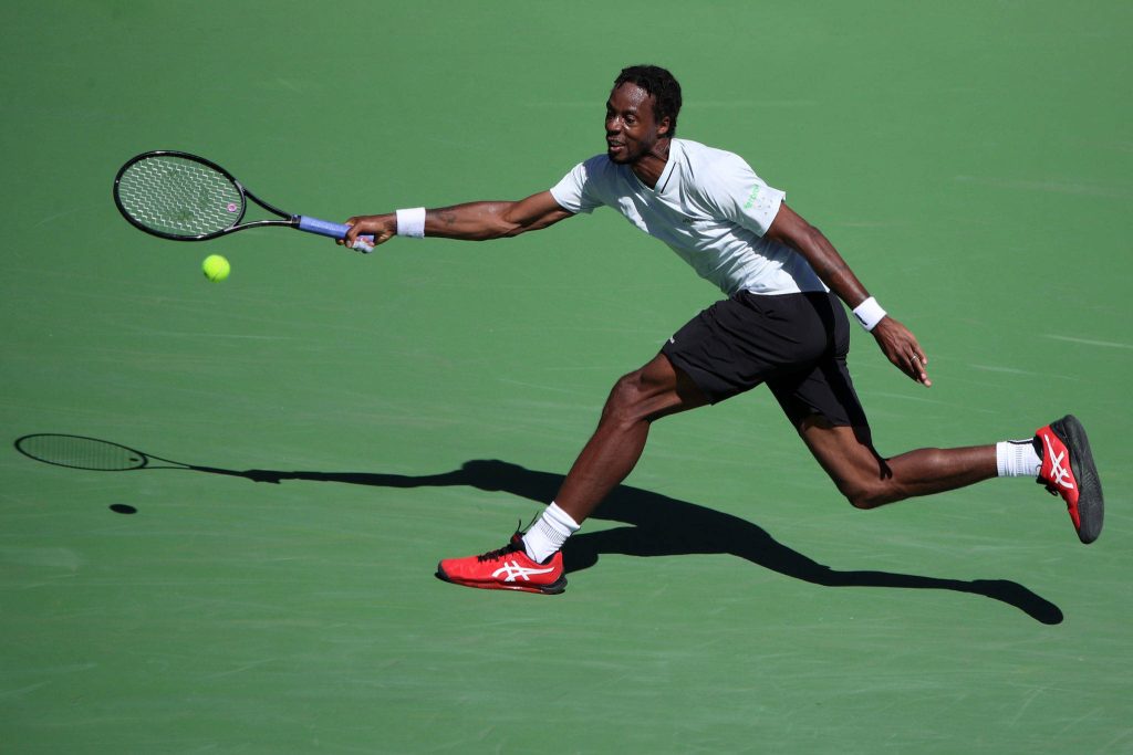 Gaël Monfils intense athletic lunge hitting return on green hard tennis court in bright sunlight Wallpaper