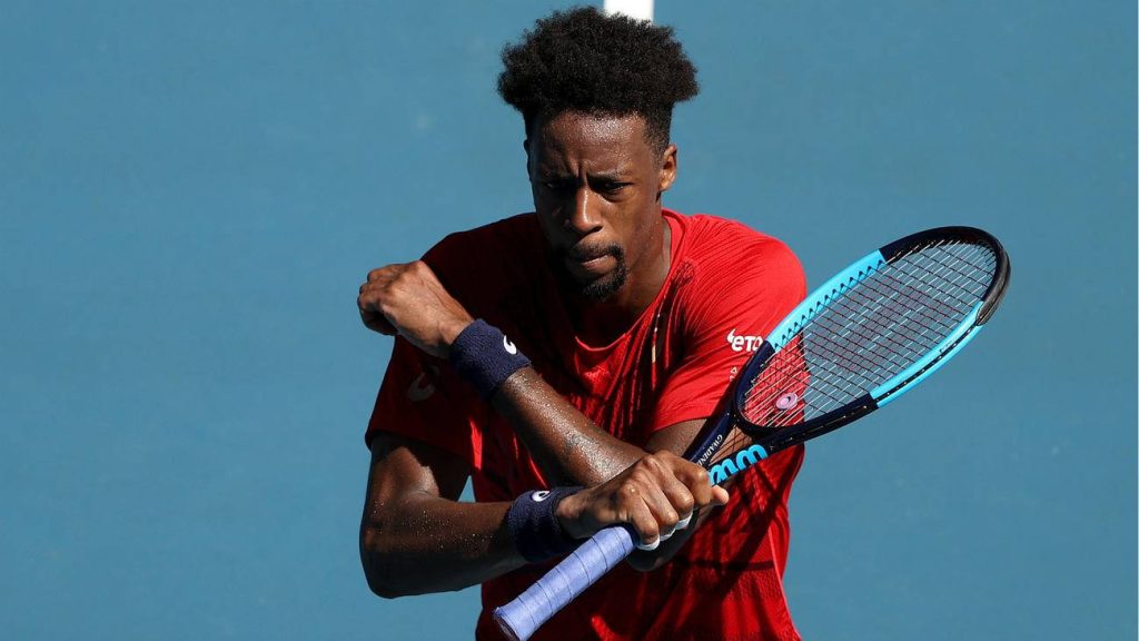 Tennis star Gaël Monfils in red shirt holding racquet arms crossed on blue court wallpaper