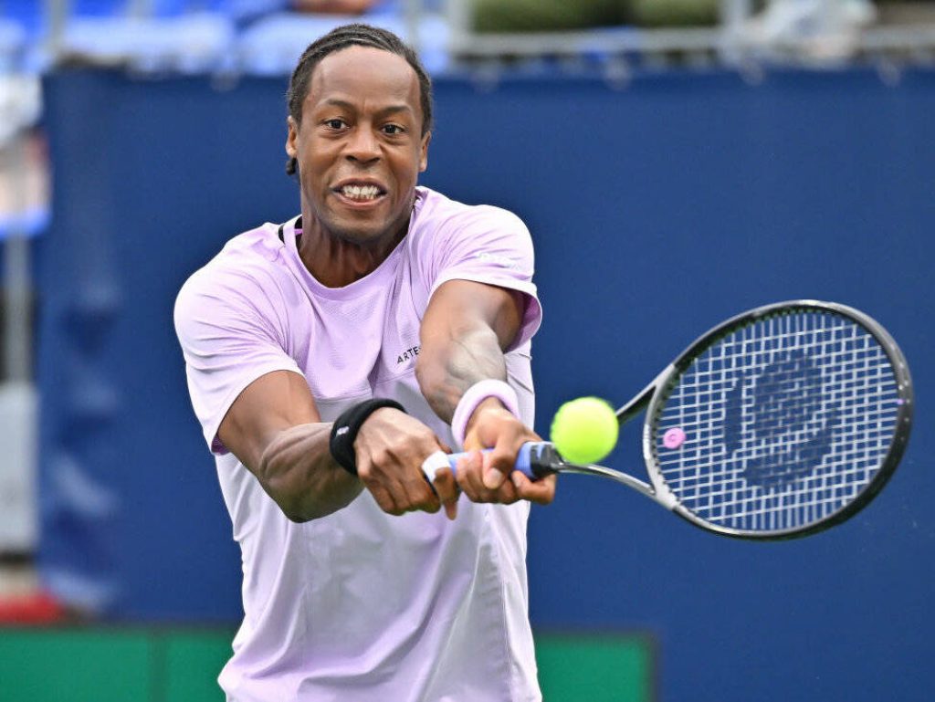 Gaël Monfils hitting a powerful two-handed backhand in pastel lavender shirt on blue court Wallpaper