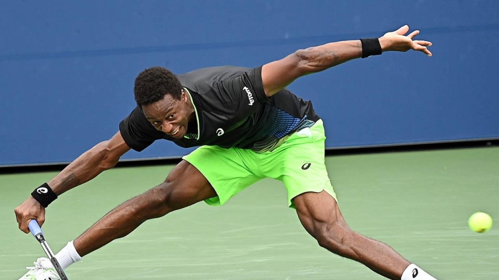 Gaël Monfils stretching wide on hard court in black kit neon green shorts intense tennis action Wallpaper