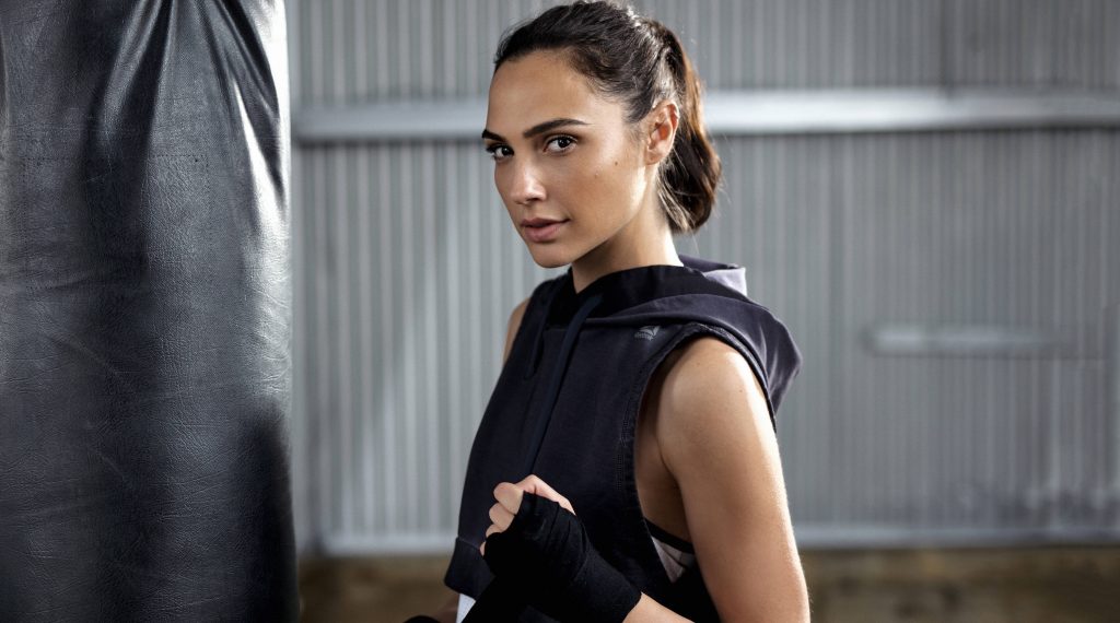 Gal Gadot confident gym pose Reebok hoodie hand wraps punching bag industrial backdrop wallpaper