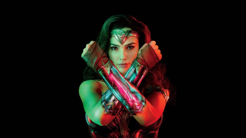 Gal Gadot as Wonder Woman striking iconic pose with red and green lighting on black background Wallpaper