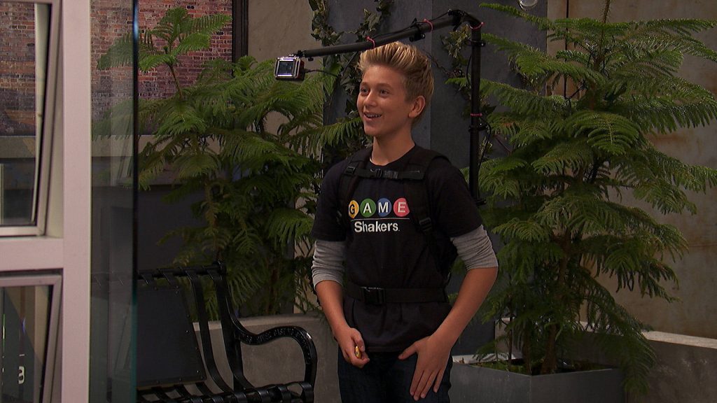 Hudson from Game Shakers in black tee with camera rig on green plant studio set wallpaper