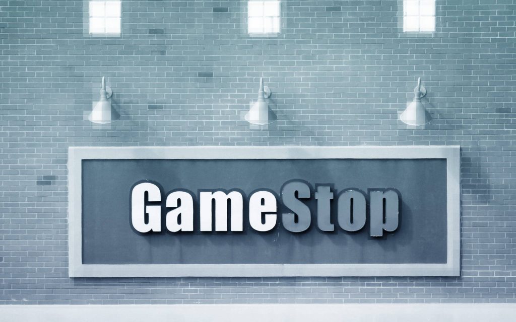 GameStop logo on gray brick wall lit by industrial sconces minimalist gaming wallpaper background