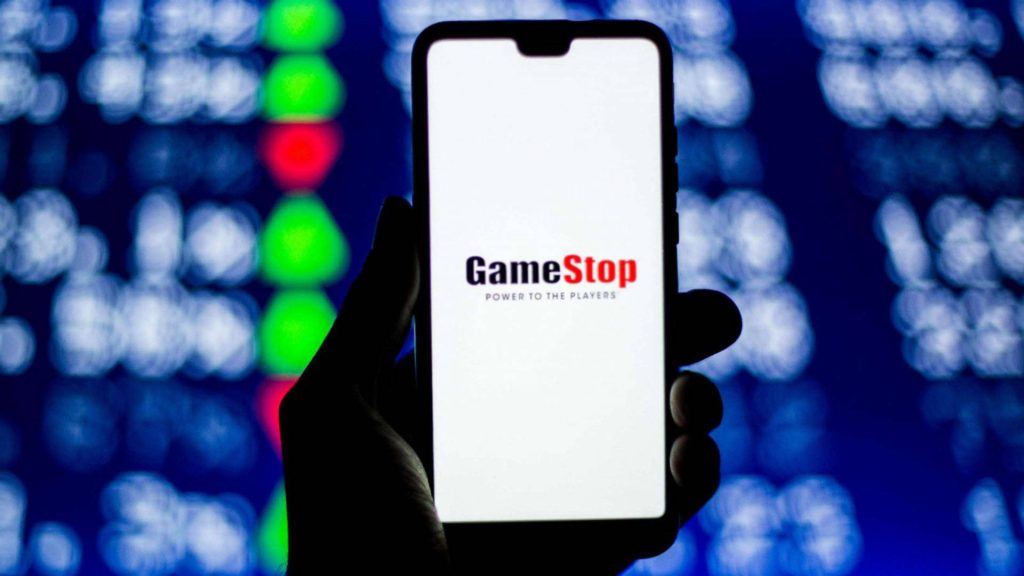 Smartphone showing GameStop logo and Power to the Players slogan on stock market background Wallpaper