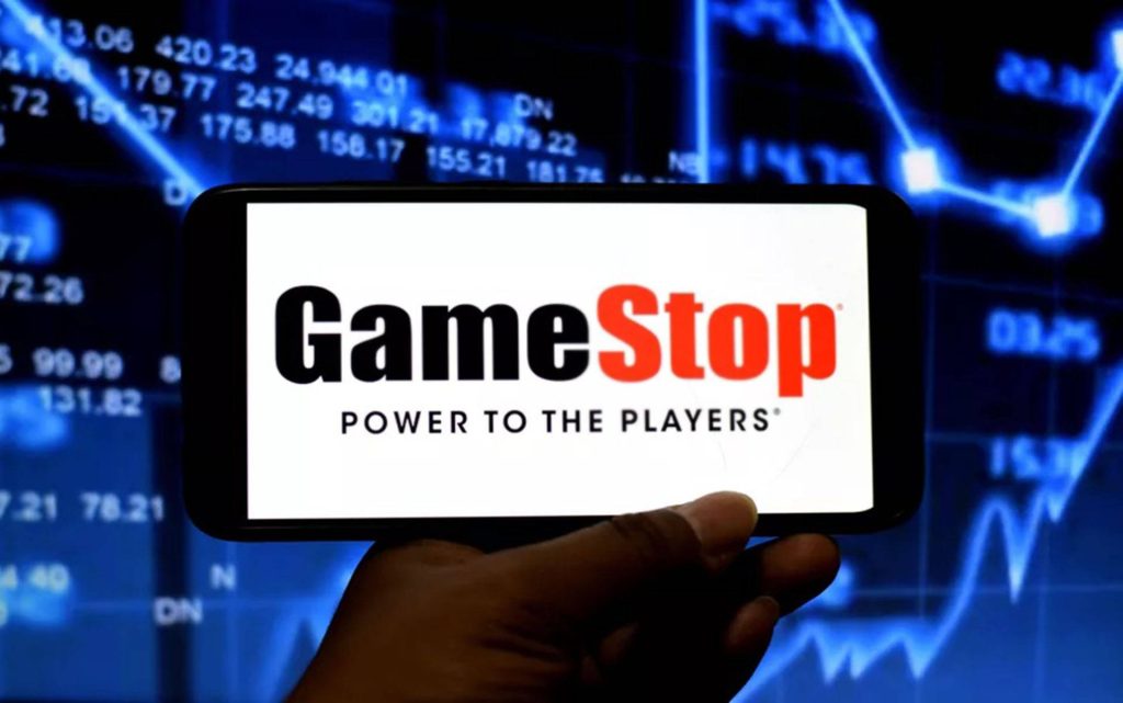 Hand holding smartphone with GameStop logo and Power to the Players on blue stock graph background Wallpaper