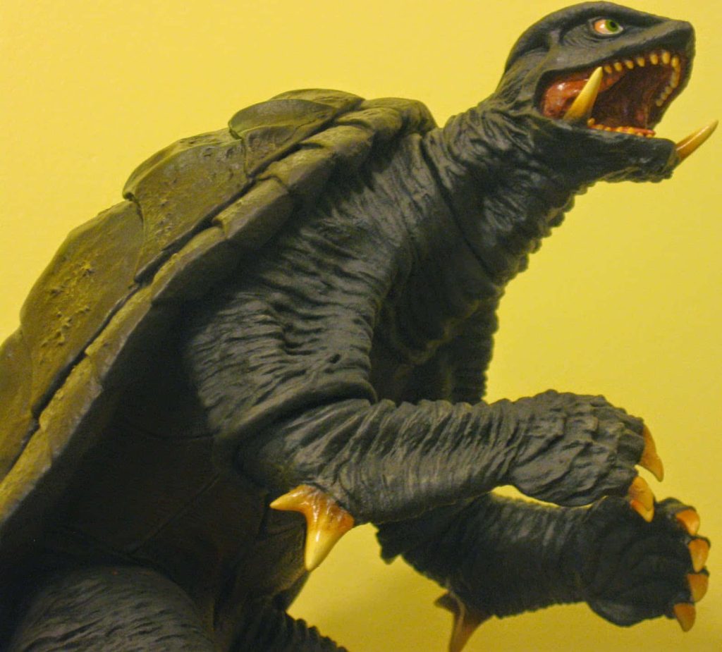 Close-up of detailed Gamera collectible figure with textured skin sharp claws and fangs yellow background Wallpaper
