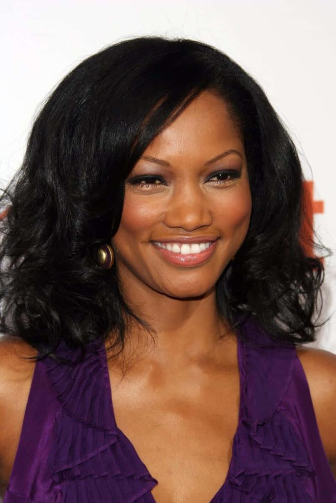 Garcelle Beauvais portrait with dark hair radiant smile purple ruffled top gold earrings elegant Wallpaper