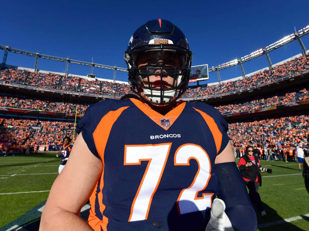Garett Bolles in Denver Broncos uniform on field with packed stadium and vivid blue sky background Wallpaper