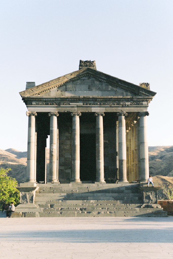 Front view of Armenia Garni Temple with Hellenistic stone columns and sunlit arid hills background Wallpaper