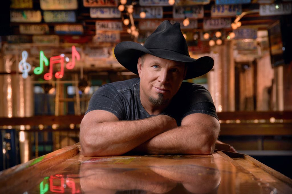 Garth Brooks in black cowboy hat at rustic bar with neon music signs and vintage plates wallpaper
