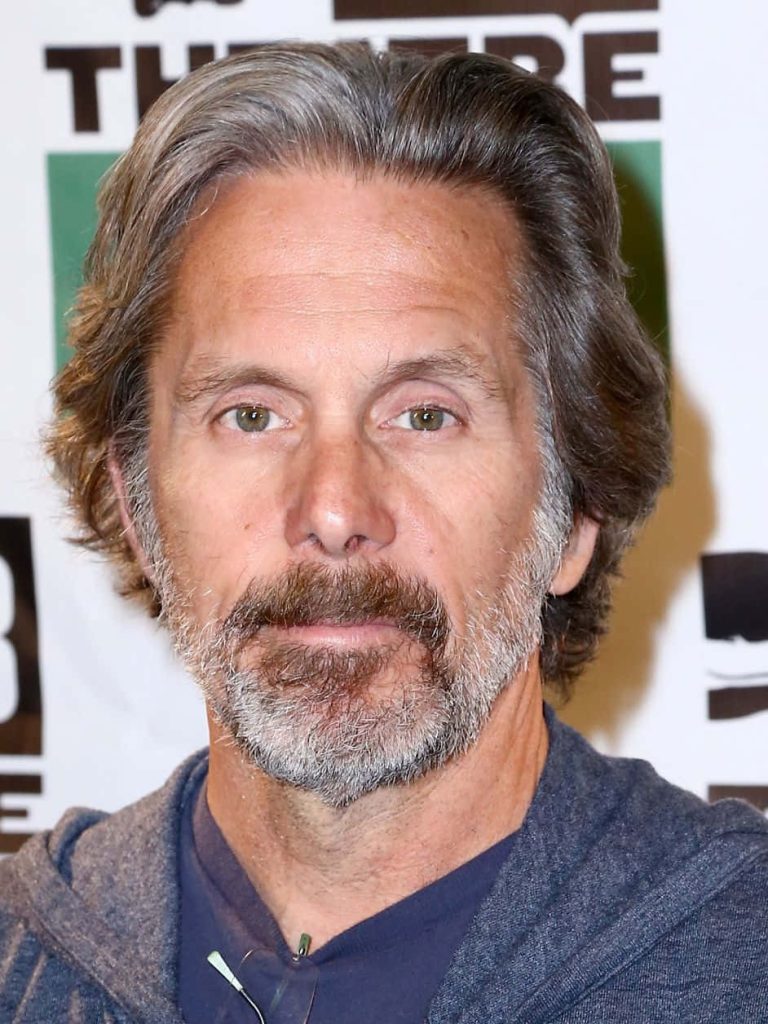Portrait of actor Gary Cole with salt-and-pepper hair and beard in blue hoodie against blurred backdrop Wallpaper