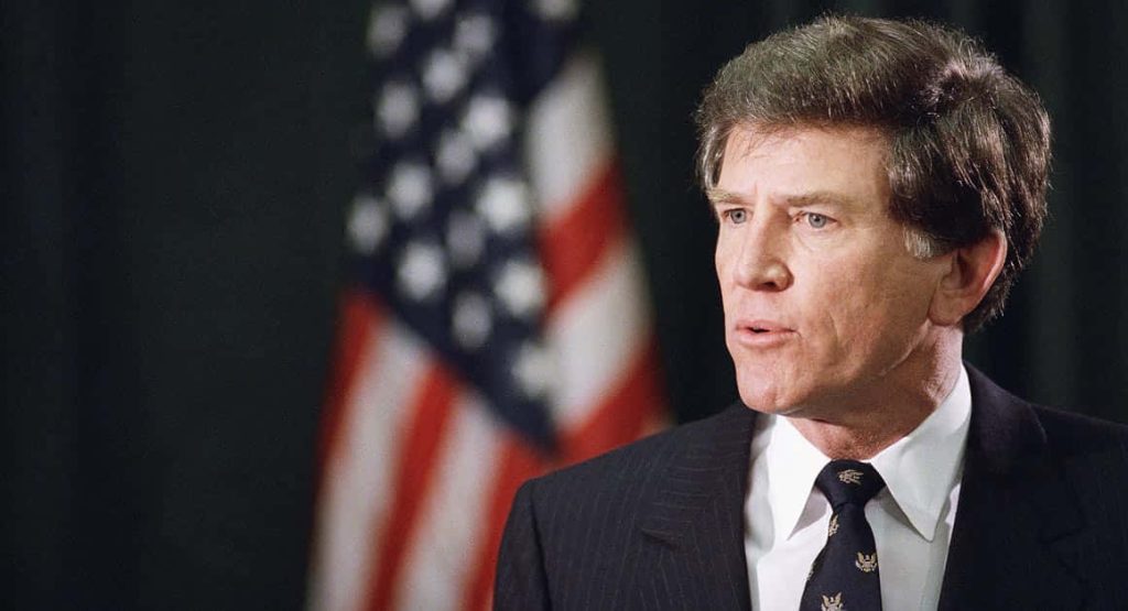 Portrait of former U.S. Senator Gary Hart in suit with soft focus American flag background wallpaper