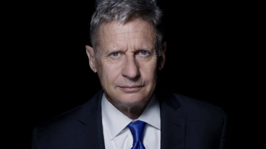 Gary Johnson portrait sharp suit blue tie high contrast black background professional lighting Wallpaper