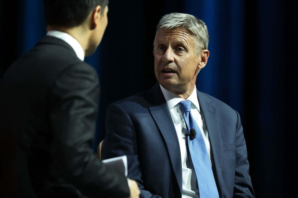 Gary Johnson in navy suit and blue tie interviewed against deep blue curtain background Wallpaper