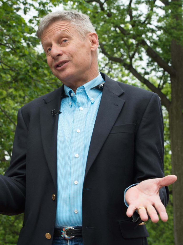 Gary Johnson in navy blazer outdoors with green foliage ideal phone wallpaper background