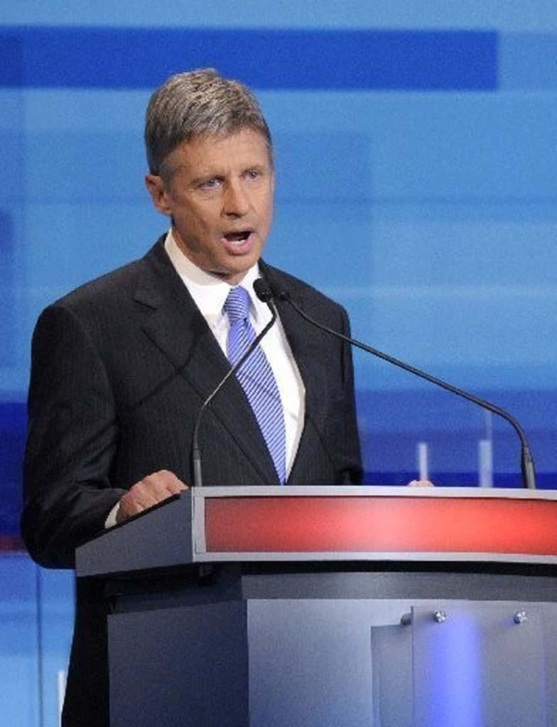 Gary Johnson delivering speech in dark suit and striped tie on bright blue political wallpaper background