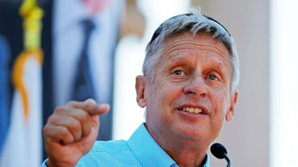 Former Governor Gary Johnson speaking at public event wearing light blue checkered shirt wallpaper background