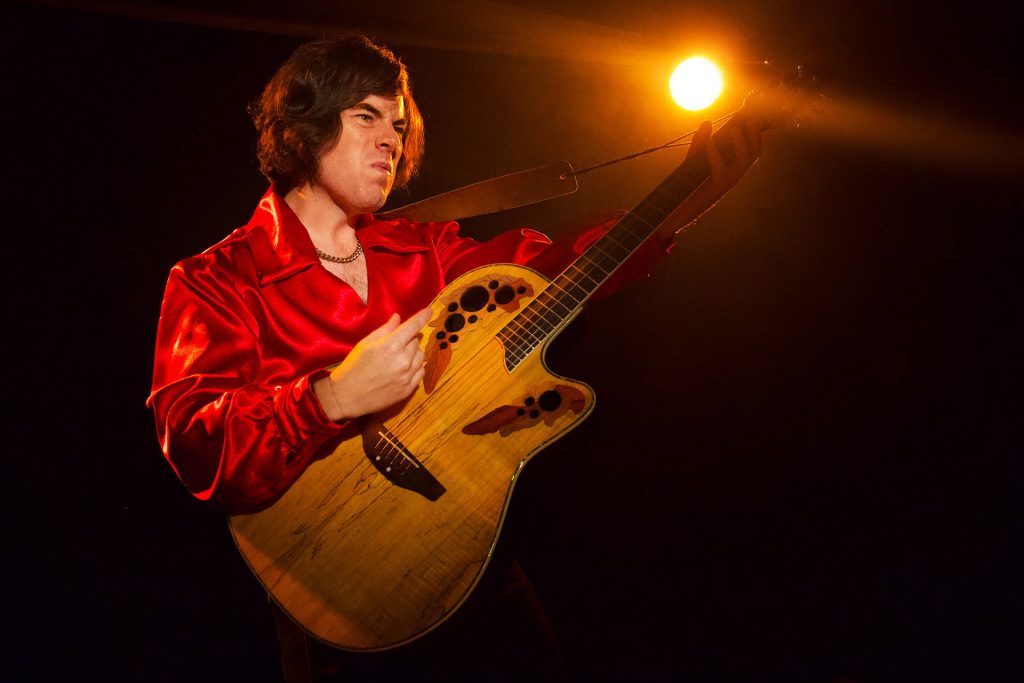 Gary Ryan performing as Neil Diamond in red shirt with Ovation guitar on dramatic stage Wallpaper