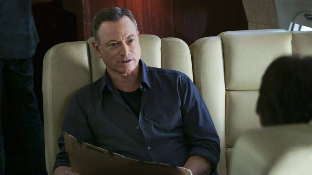 Gary Sinise serious in dark shirt holds file seated in cream leather airplane seat cinematic wallpaper