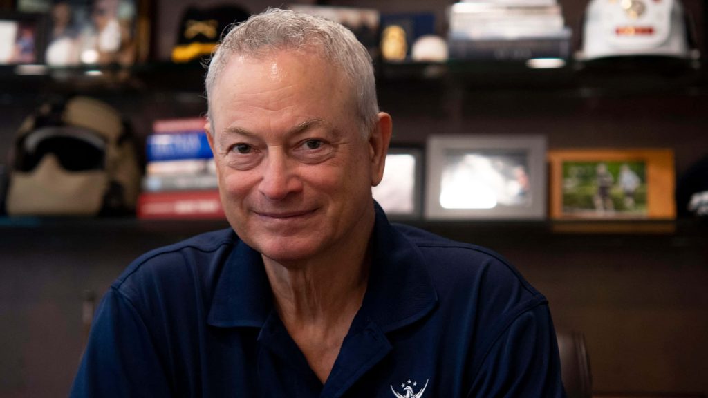 Gary Sinise smiling in navy polo with foundation logo military memorabilia background portrait Wallpaper