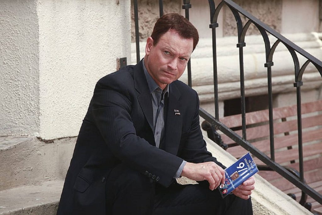 Gary Sinise holds 9/11 memorial booklet in dark suit on concrete steps outdoor portrait professional Wallpaper