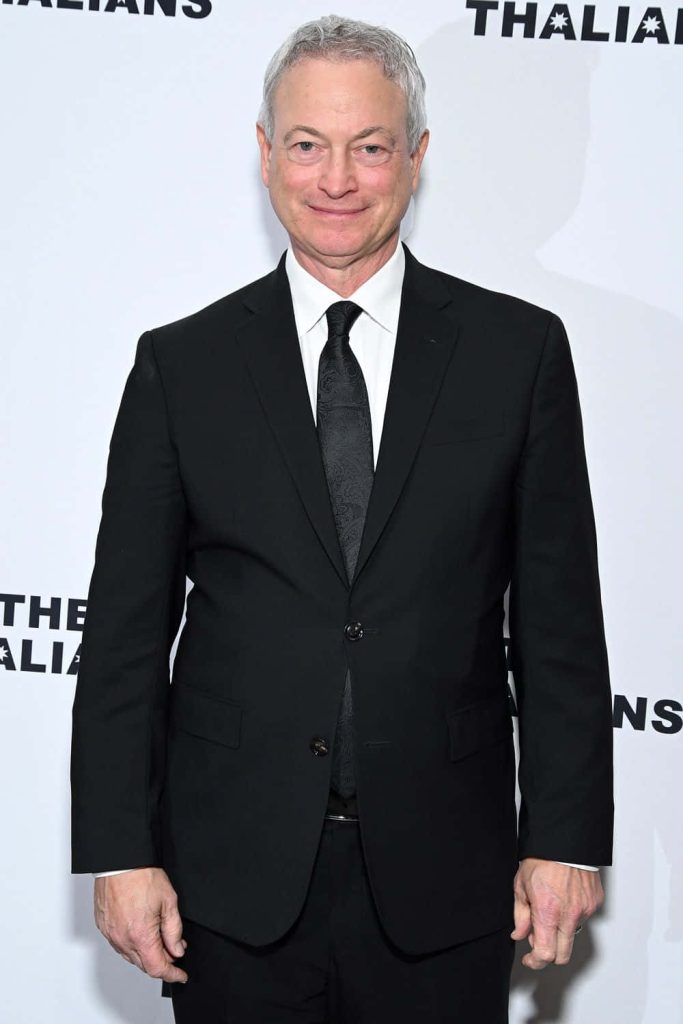 Gary Sinise portrait in black suit white shirt textured tie on bright white event backdrop wallpaper
