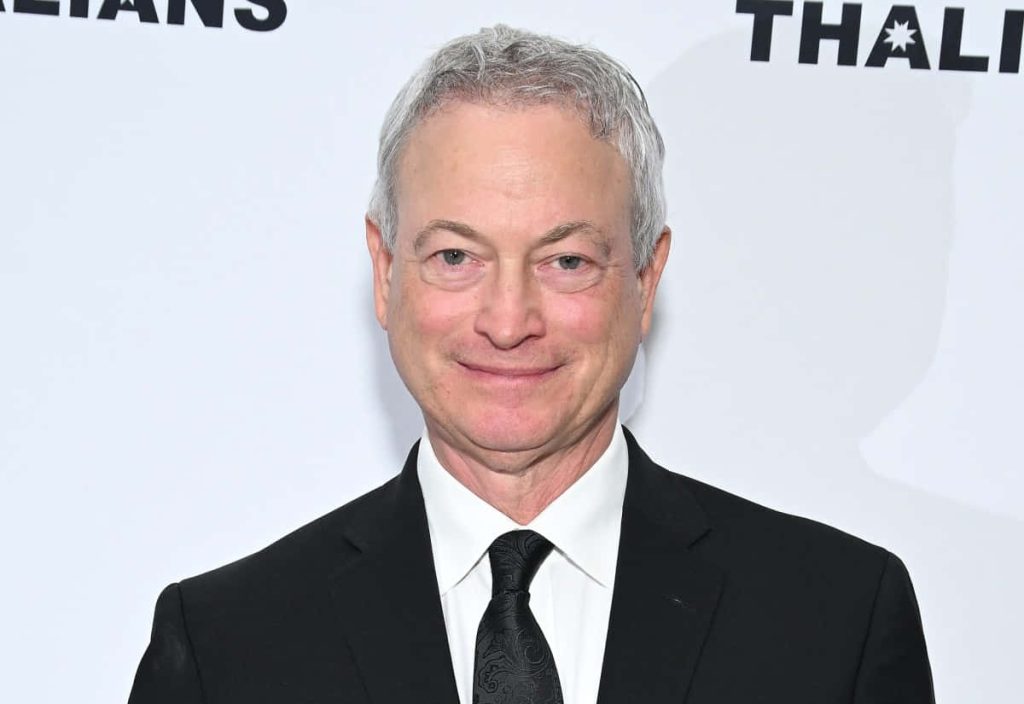 High-resolution portrait of Gary Sinise smiling in a black suit white shirt and patterned tie Wallpaper