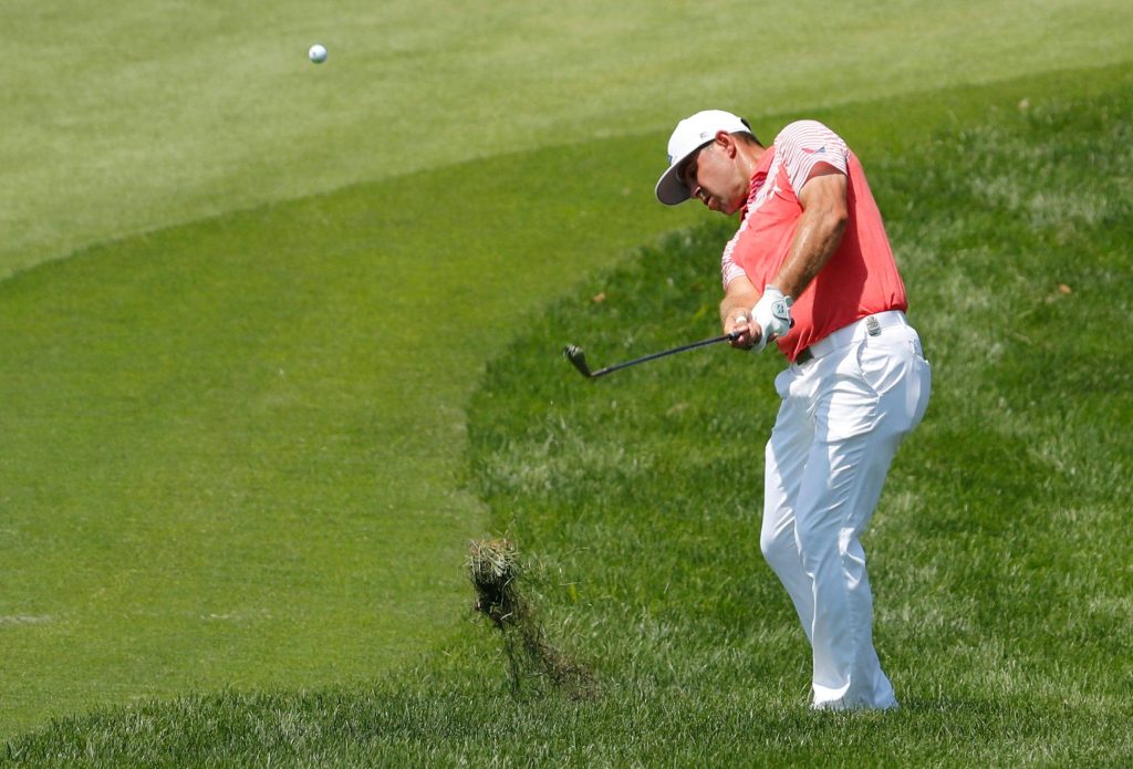 Professional golfer Gary Woodland hitting a powerful golf shot from the rough on lush course Wallpaper