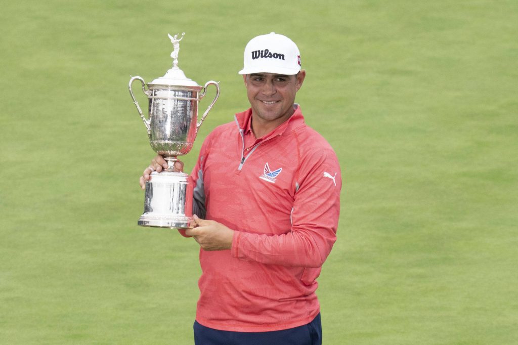 Gary Woodland lifting U.S. Open trophy on green golf course in coral pullover and white cap Wallpaper
