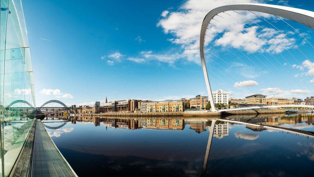 Gateshead Millennium Bridge and Tyne Bridge over River Tyne with clear reflections and blue sky Wallpaper