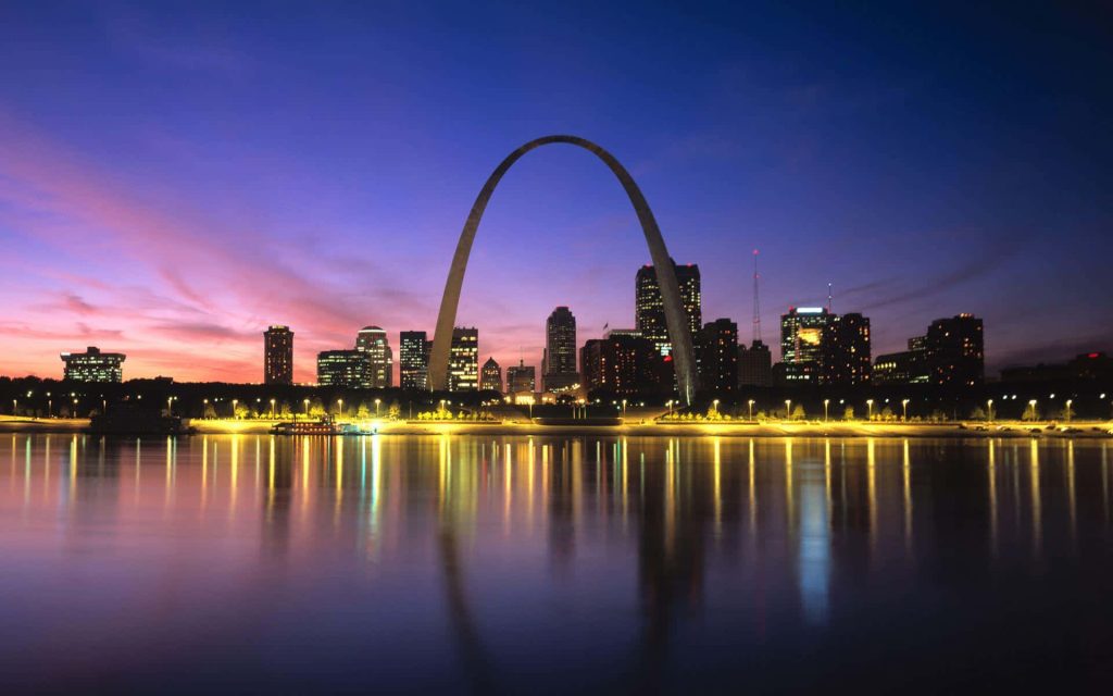 Gateway Arch at night with purple pink sky and St Louis city skyline reflecting on Mississippi River