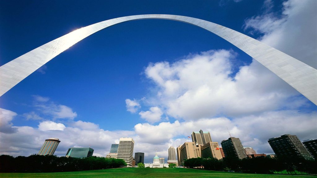 Low-angle view of Gateway Arch in St Louis with city skyline and blue sky wallpaper background