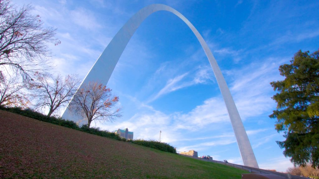 Gateway Arch towering over green park hills and trees under a bright blue sky wallpaper background