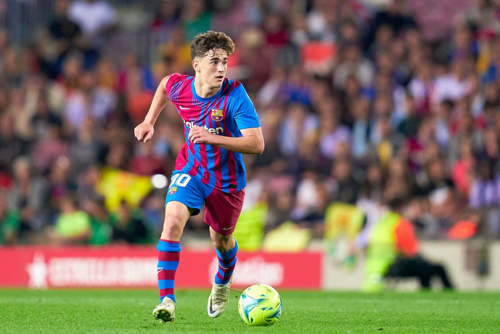 FC Barcelona midfielder Gavi dribbling ball in blue red kit with blurred stadium crowd background Wallpaper