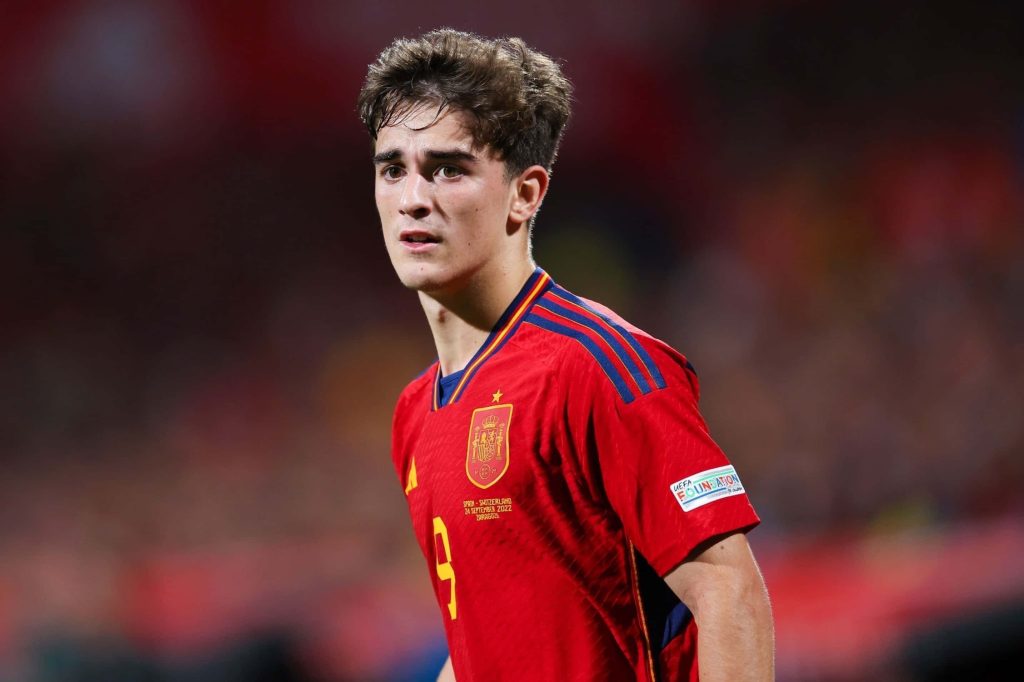 Gavi in red Spain jersey focused during match with blurred stadium background wallpaper background