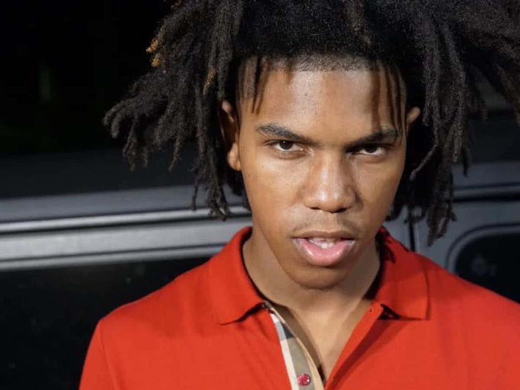 Portrait of rapper Gee Money in red polo shirt with dreadlocks against dark moody background Wallpaper
