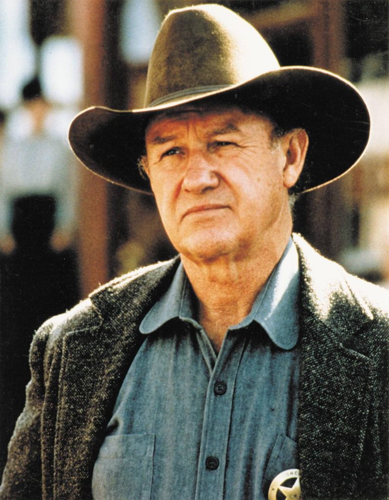Gene Hackman as stern sheriff in cowboy hat and coat cinematic Western movie wallpaper background