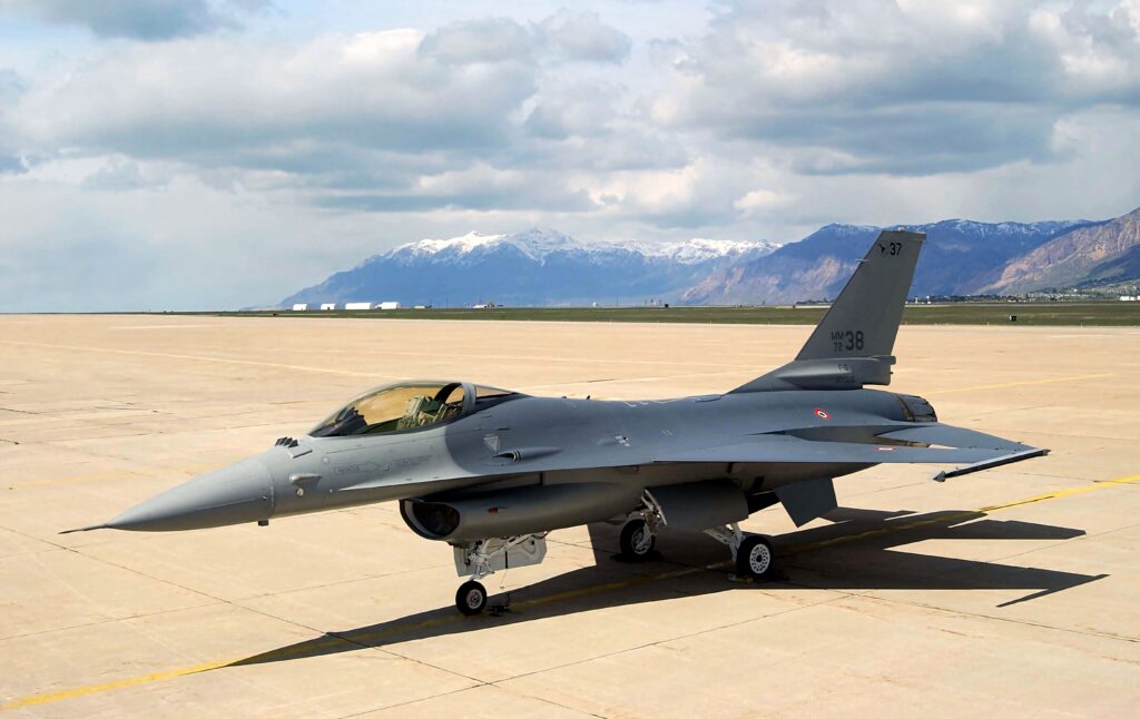 General Dynamics F-16 Fighting Falcon jet on sunlit runway with gray camouflage and mountain backdrop Wallpaper