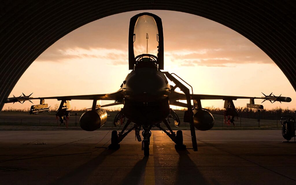 Silhouette of General Dynamics F-16 Fighting Falcon inside hangar at sunset showcasing sleek design Wallpaper